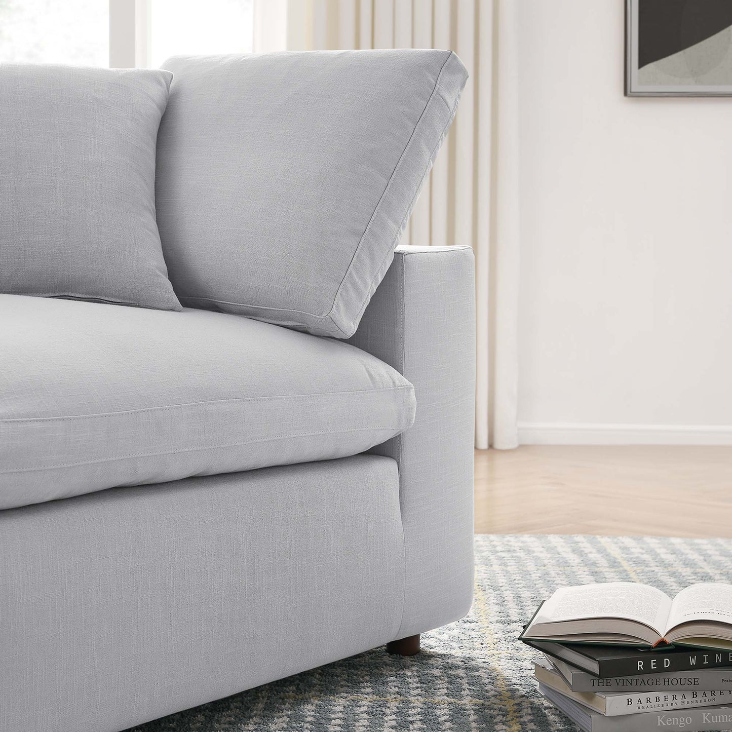 Light gray fabric corner chair with overstuffed cushions and modern arms on a blue patterned rug; open book and magazines beside.