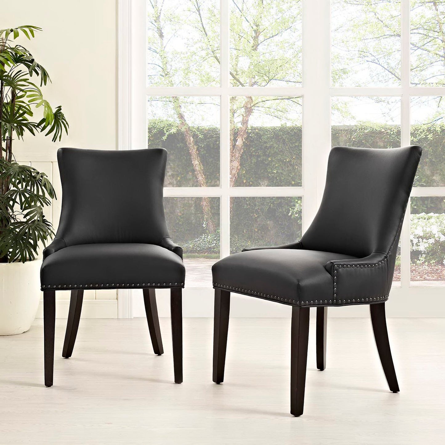 Two black faux-leather dining chairs with nailhead trim and dark wood legs in a bright room.