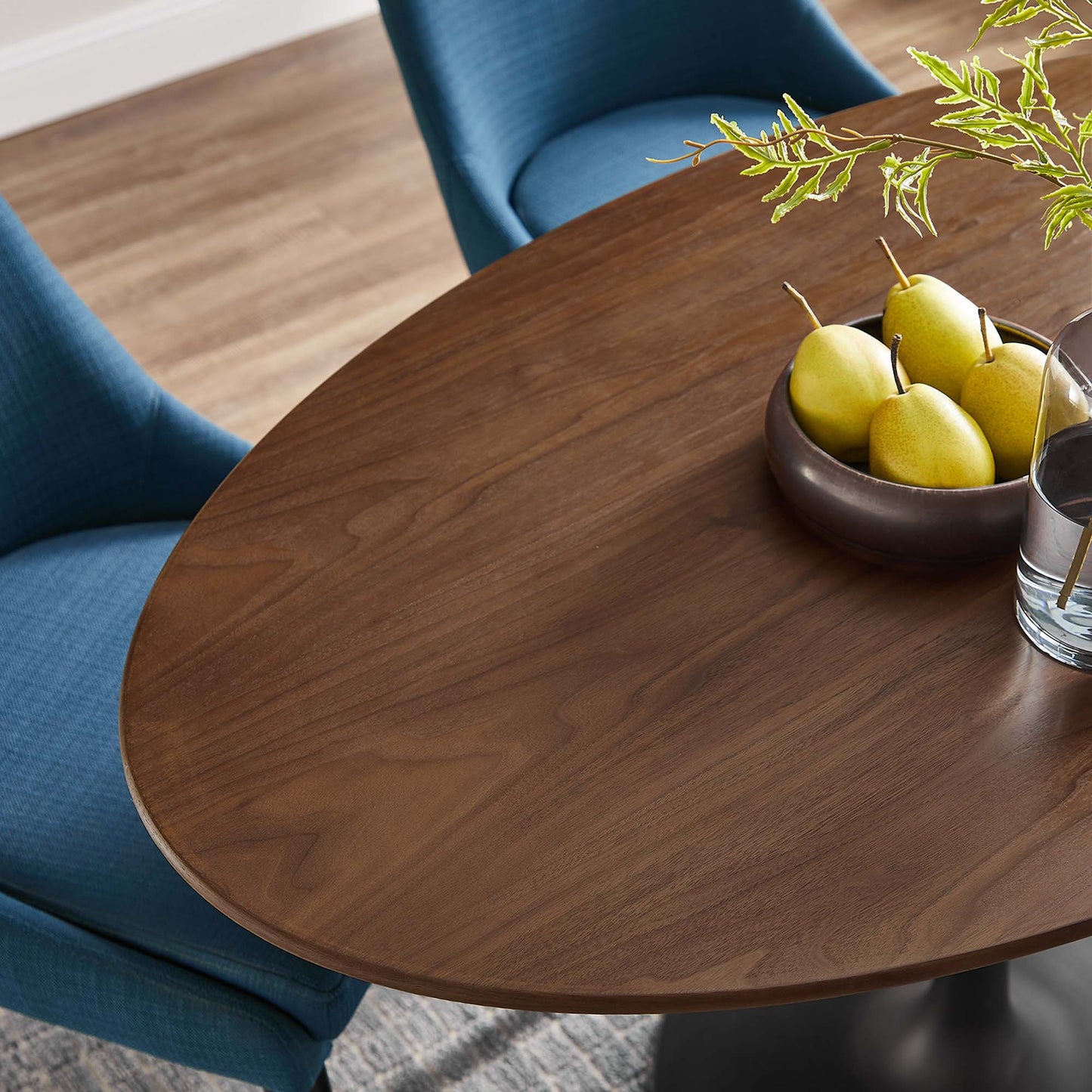 Walnut oval dining table with pedestal base (48") and a bowl of pears with greenery as a centerpiece.