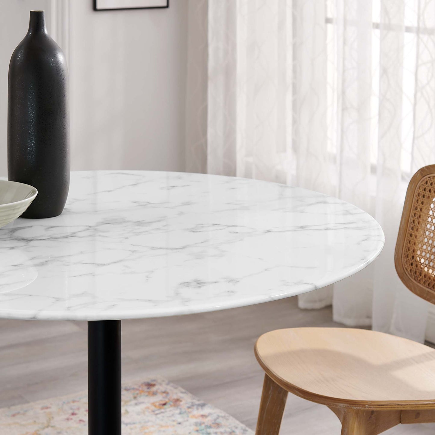 Round faux marble top with gray veins on a black metal base, black vase and a light wood chair with a cane back.