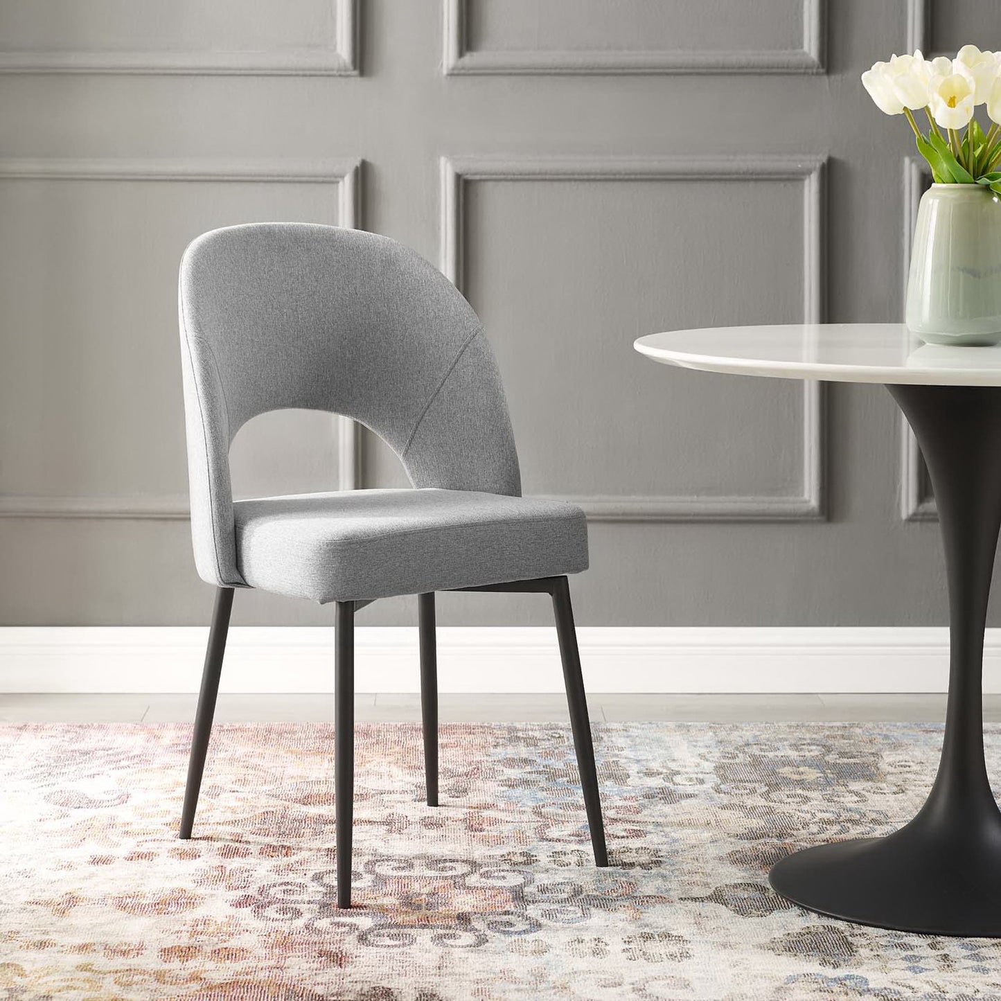 Light gray upholstered dining chair with curved back and black legs beside a round white table with a black pedestal.