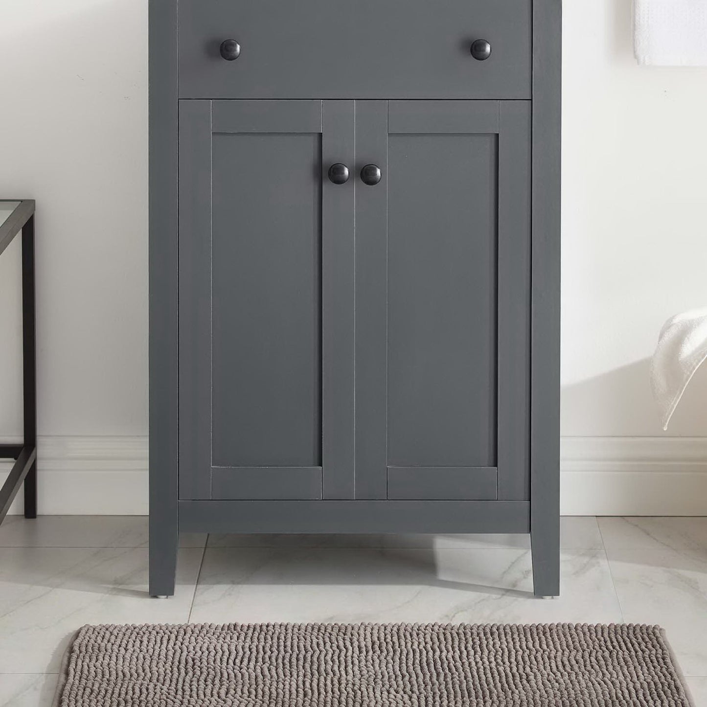 Gray bathroom vanity cabinet with two panel doors, dark round knobs, and tapered legs.