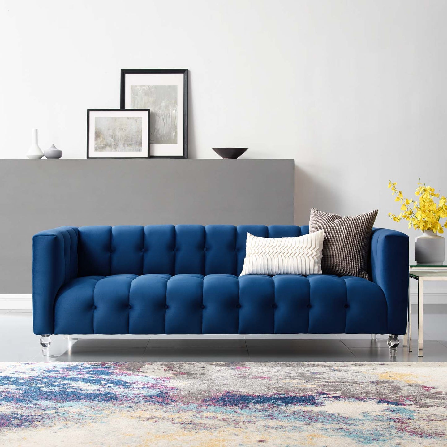 Navy blue tufted velvet sofa with chrome legs in a modern living room; two throw pillows.
