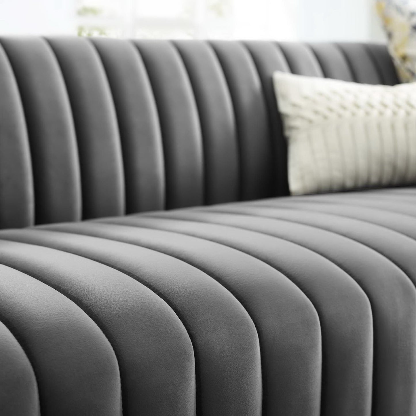 Grey velvet sofa with vertical channel tufting and a white textured pillow.