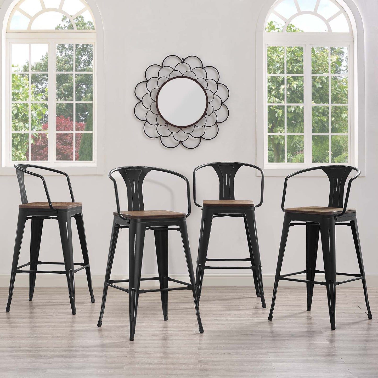Four black metal bar stools with brown wooden seats in a bright room with arched windows and a round flower-shaped mirror.
