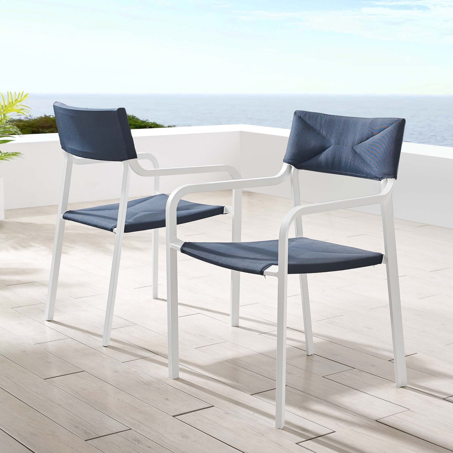 Outdoor white aluminum armchairs with navy cushions and back pillows around a white table on a seaside terrace (set of 2).