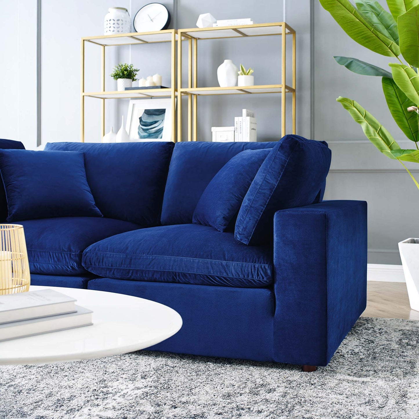 Navy velvet loveseat with plush cushions in a modern living room; gold metal shelves, green plant, and a white round coffee table.