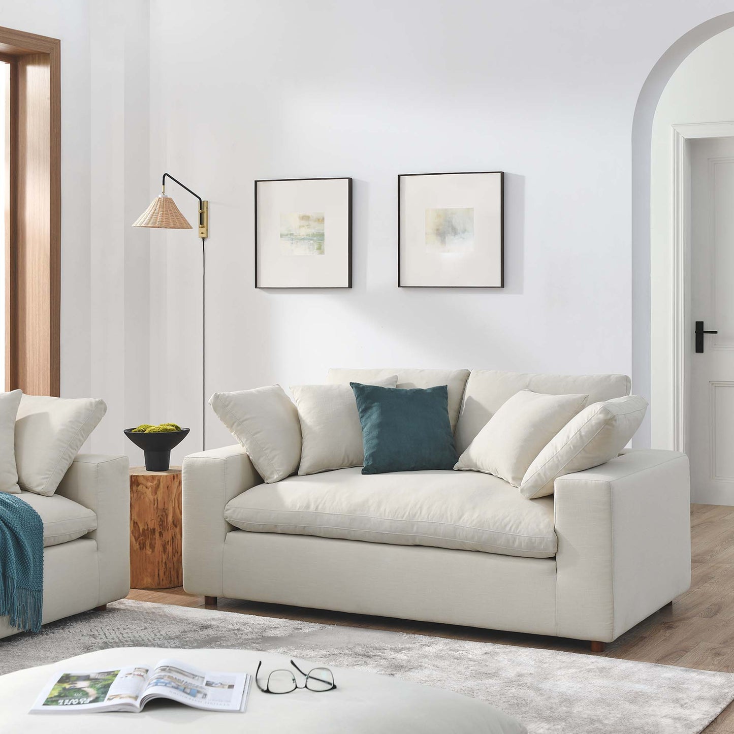 Beige modern loveseat with teal accent cushion in bright living room; two framed prints, wood stump side table, arch doorway.