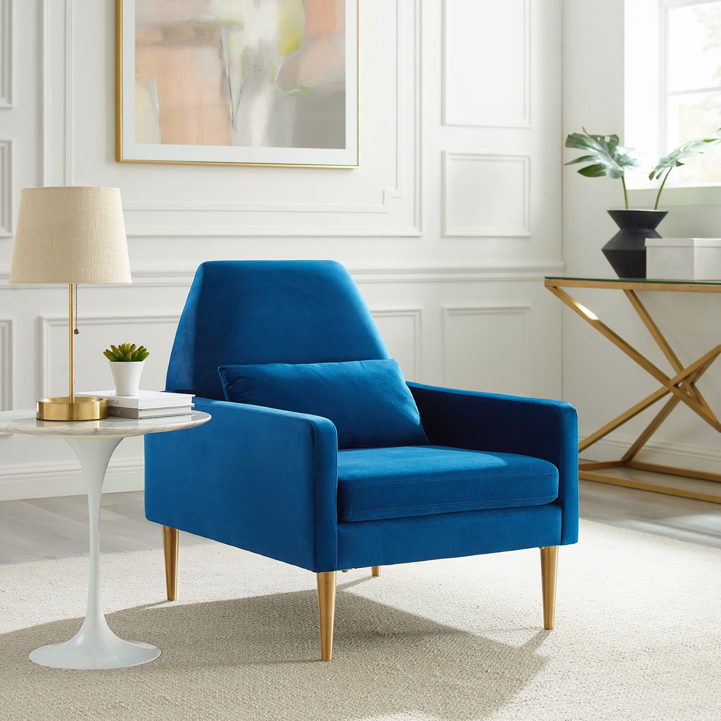 Navy velvet armchair with gold tapered legs and matching cushion in a bright white-paneled living room.