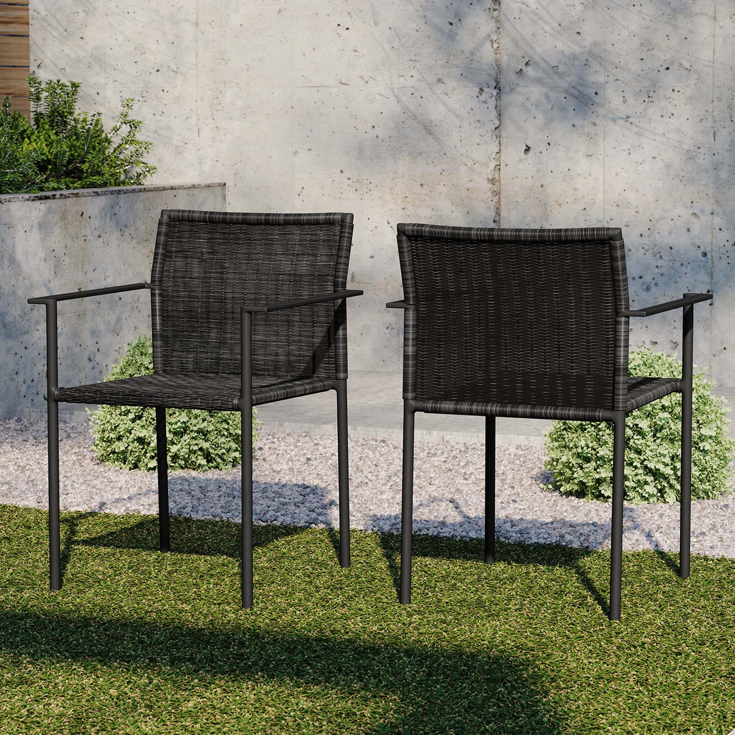 Two dark wicker outdoor armchairs with metal frames on a grassy patio against a concrete wall.