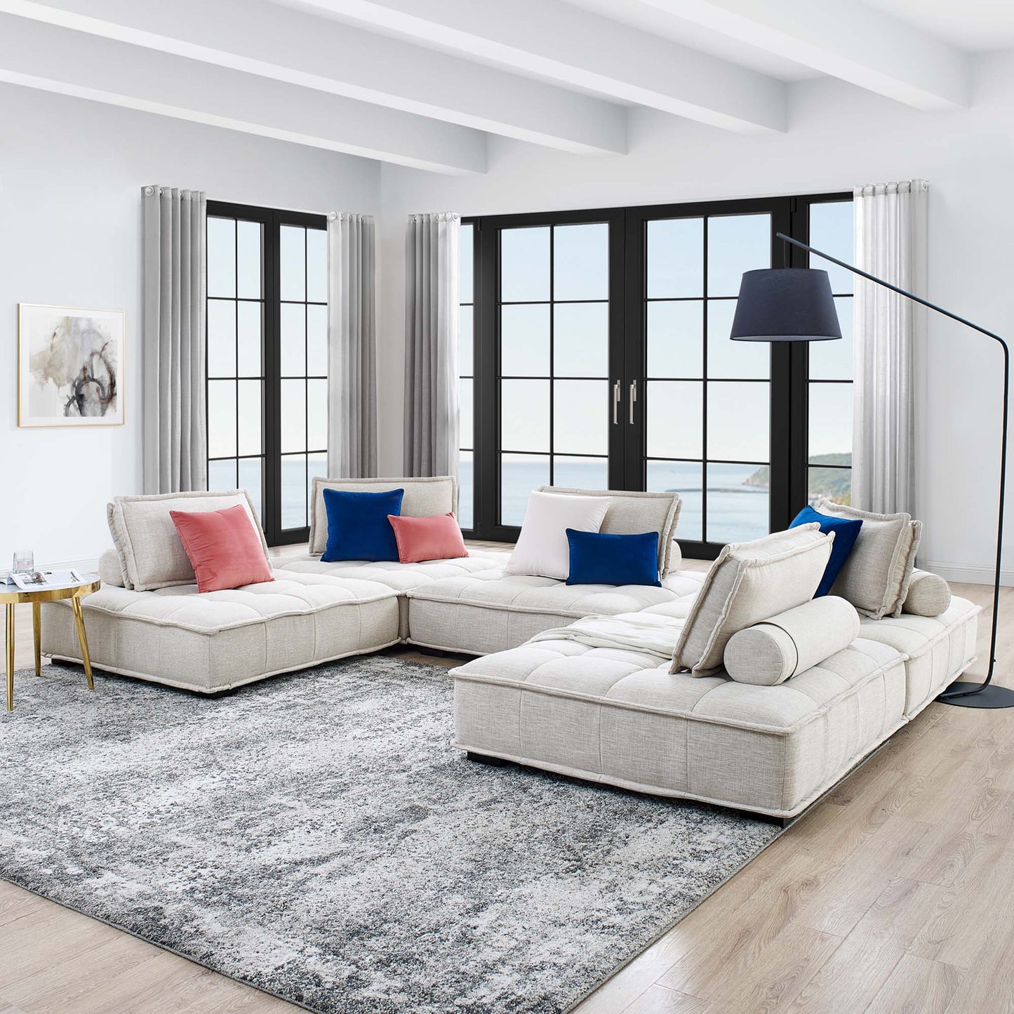Brown modular sectional with chaise in a living room; tufted fabric upholstery, black-framed windows, and a curved blue floor lamp.