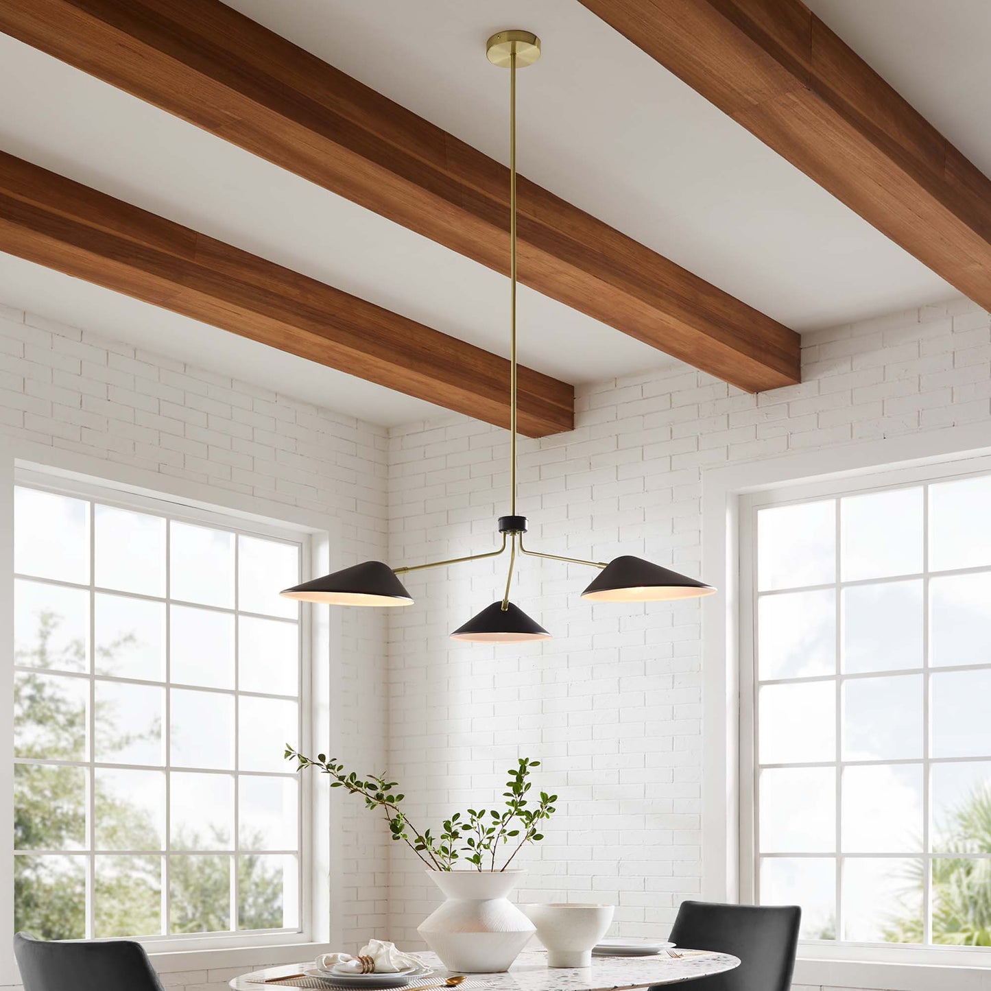 Three black cone pendant light with brass stem over white dining table; exposed wood beams & white brick walls.