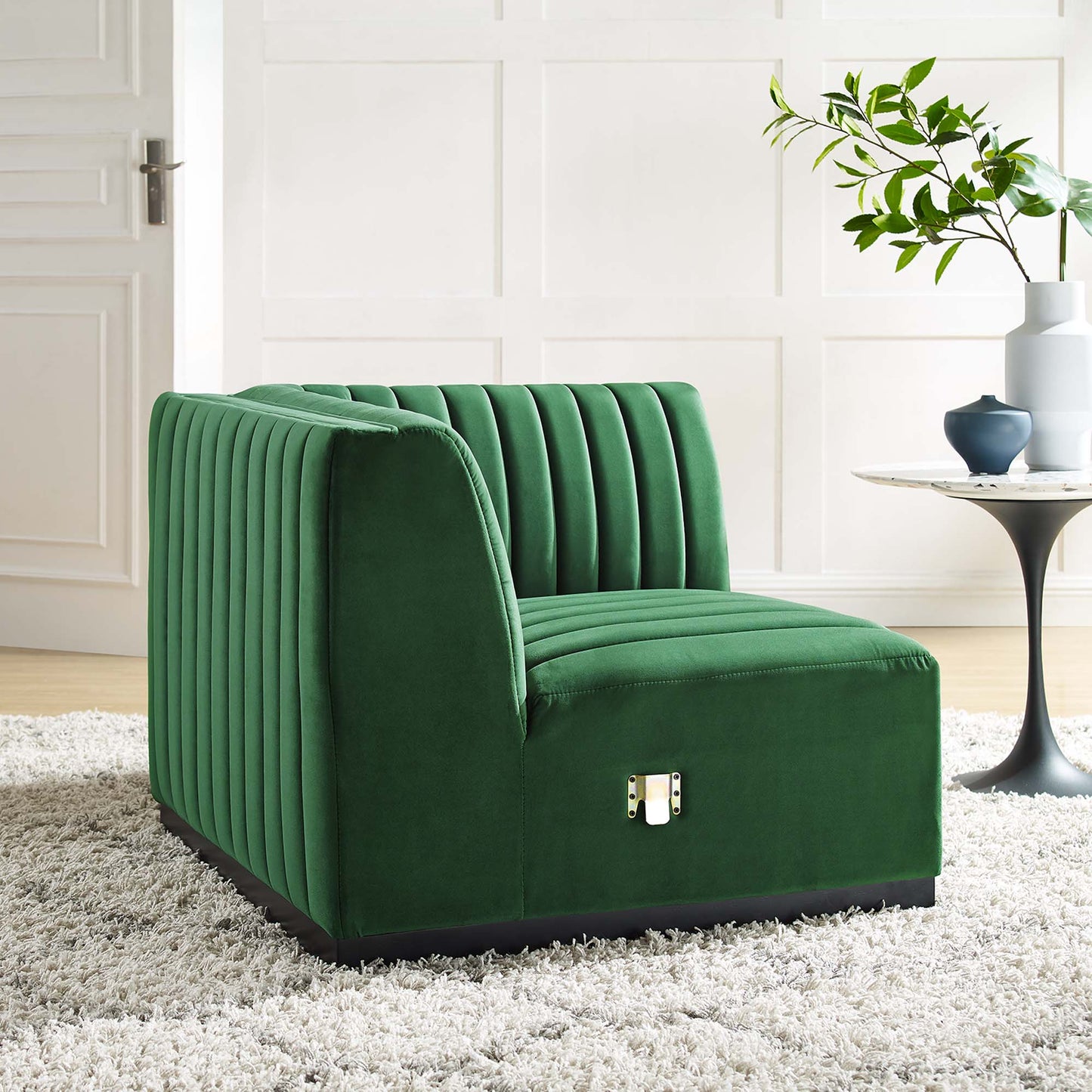 Emerald green velvet right-corner chair with vertical channel tufting, modern boxy arms, and a low black base in living room.