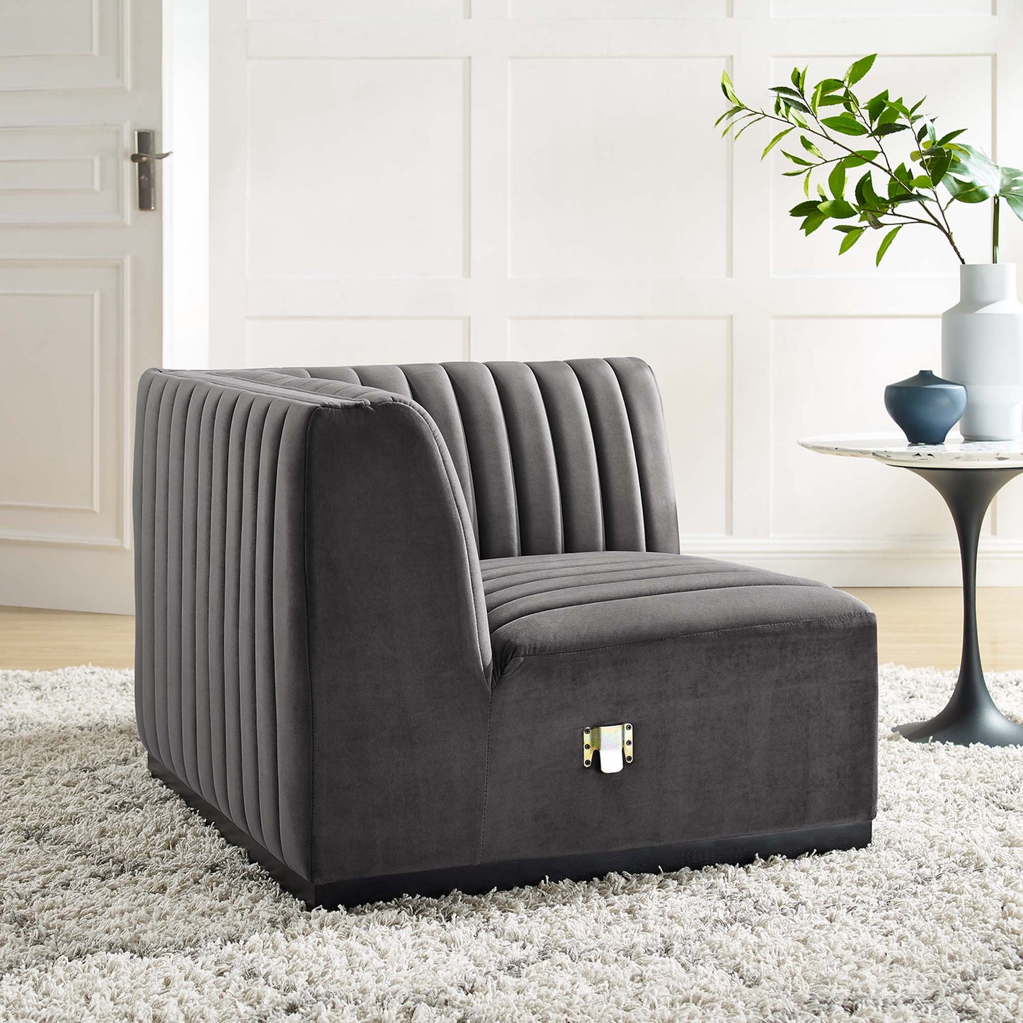 Charcoal gray velvet corner chair with vertical channel tufting, low-profile square arms, in a bright minimalist room.