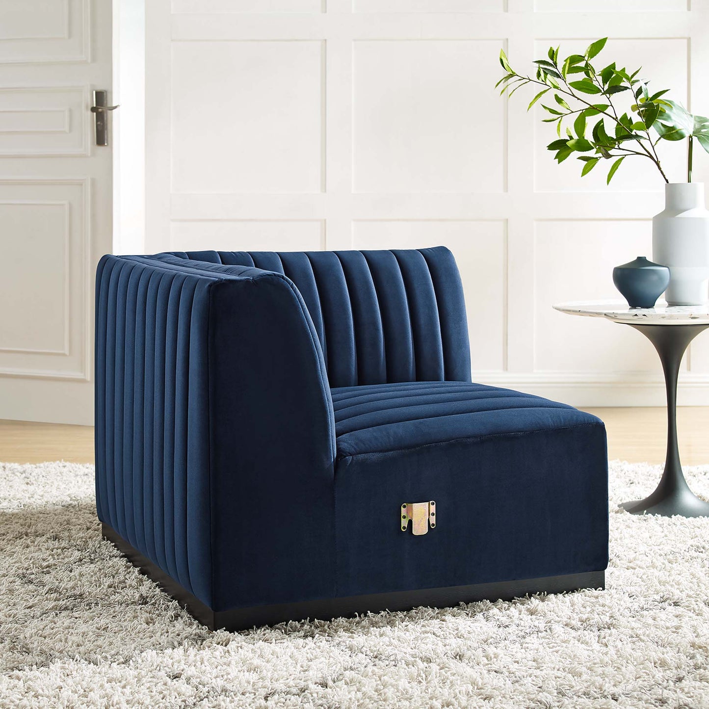 Midnight blue velvet, vertical-channel tufted right-corner chair with a low profile and dark base in a white, paneled living room.