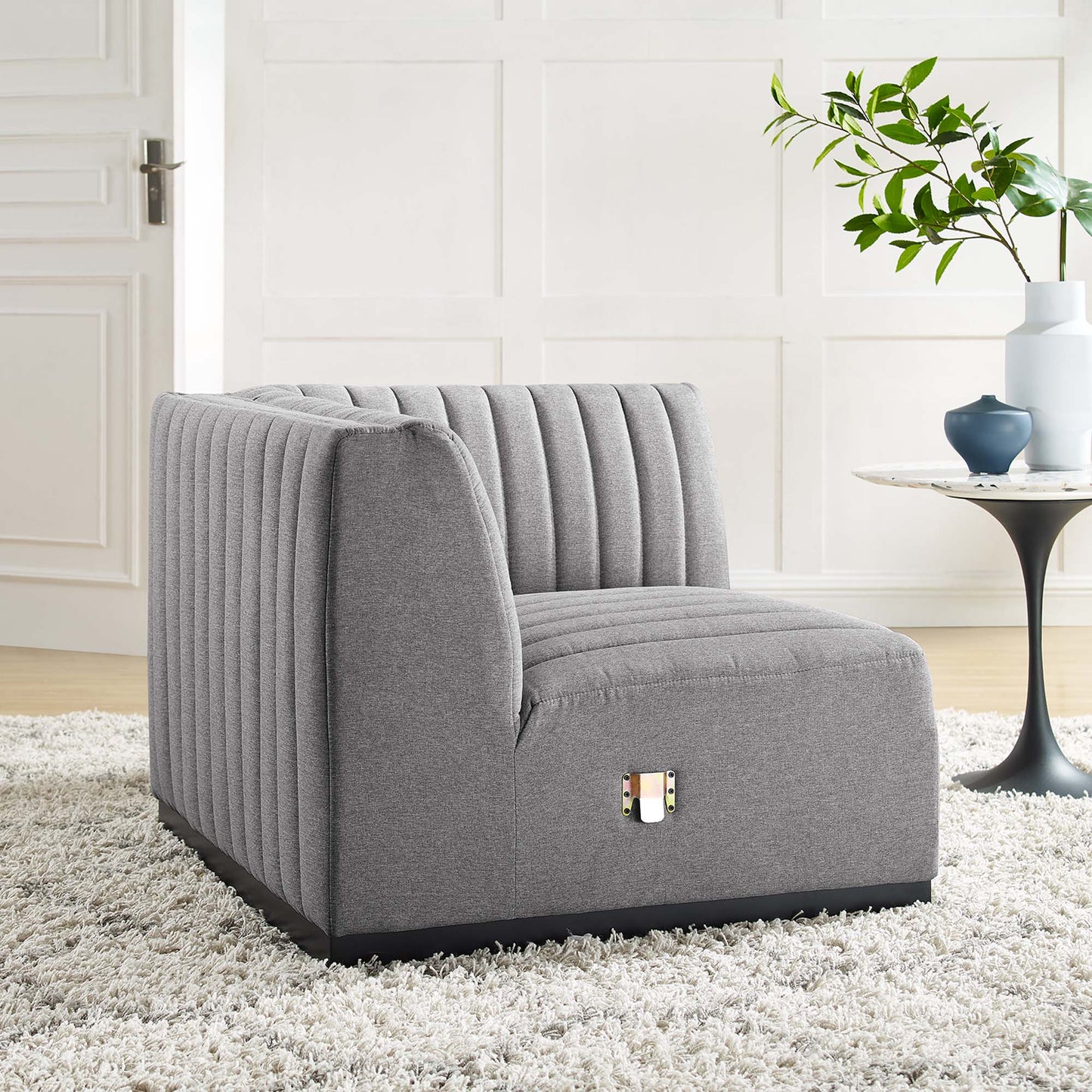 Gray upholstered lounge chair with vertical channel tufting and black base in a bright living room.
