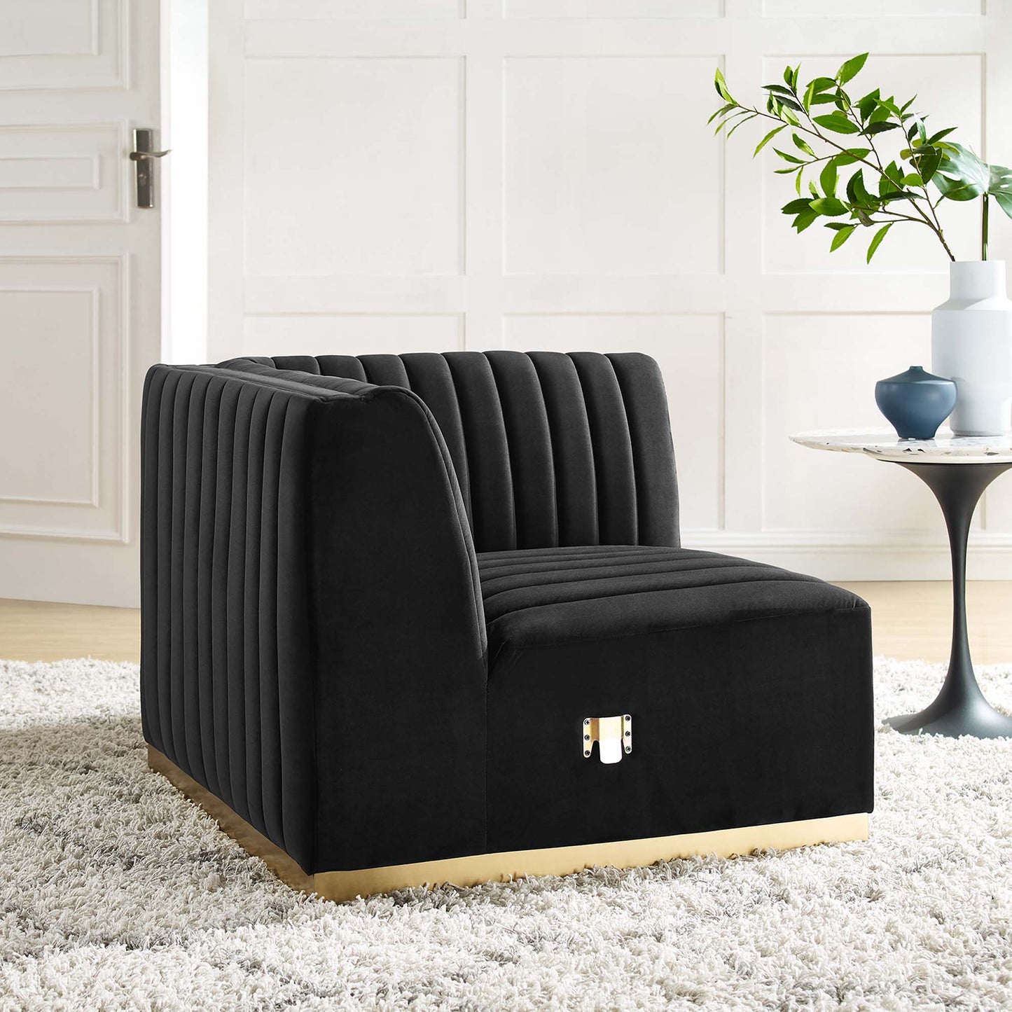 Black velvet channel-tufted right corner chair with gold base in a modern living room.