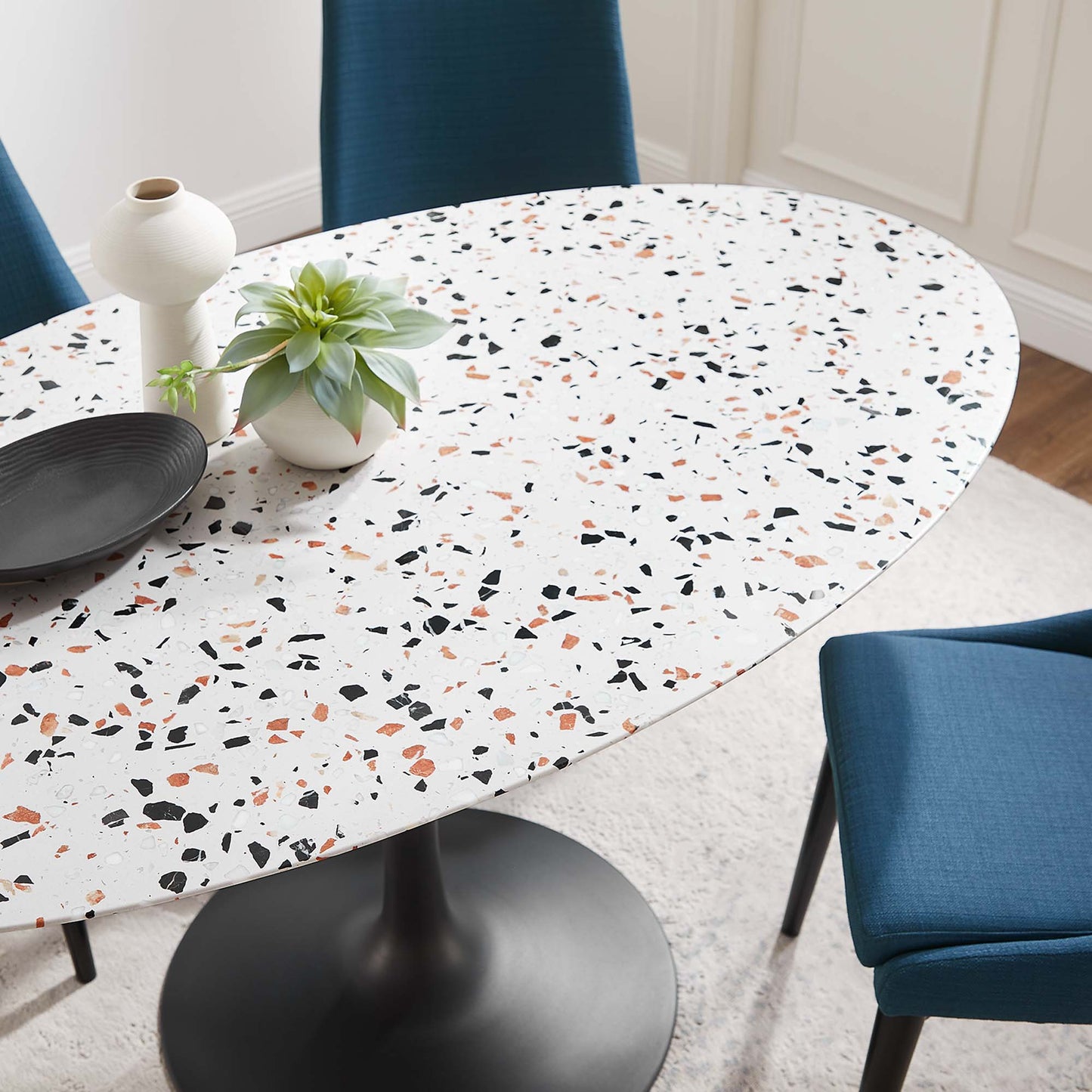 Terrazzo oval dining table with a white-speckled surface in black, orange and green chips; dark pedestal base, chairs.