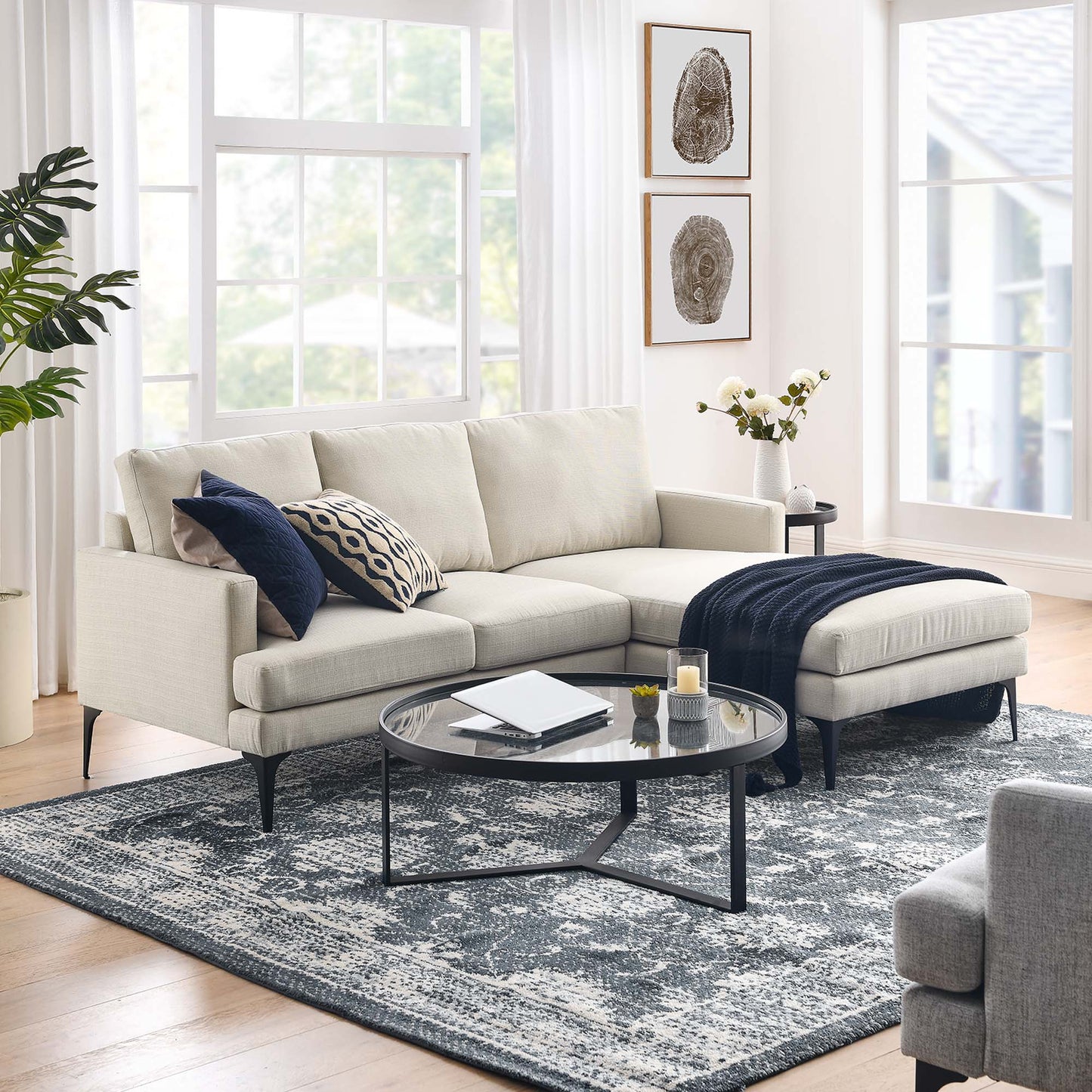 Beige sectional with chaise, navy throw, round glass coffee table; blue-gray patterned rug in a bright living room.