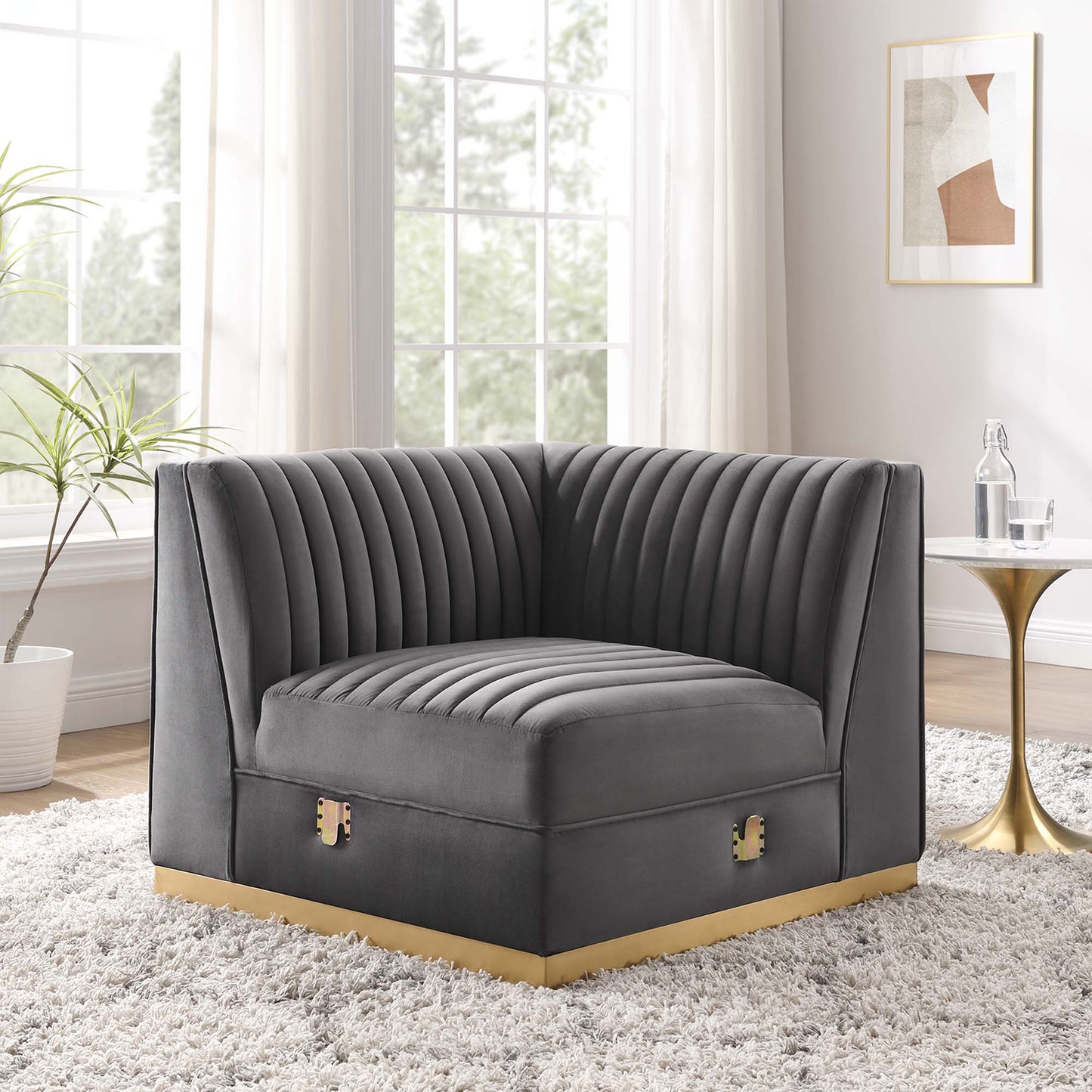 Gray velvet modular sectional sofa left corner chair with vertical channel tufting and gold-tone base trim in a bright living room.