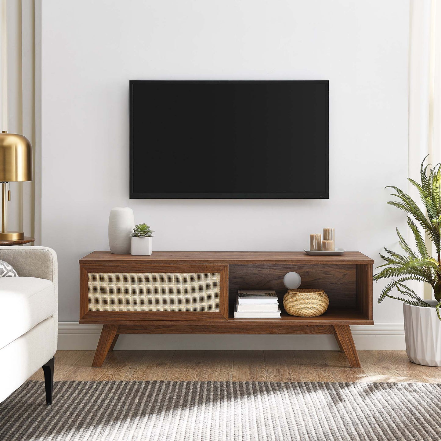 Walnut mid-century media console with woven front panel, open shelf, decor; wall-mounted flat-screen TV above.