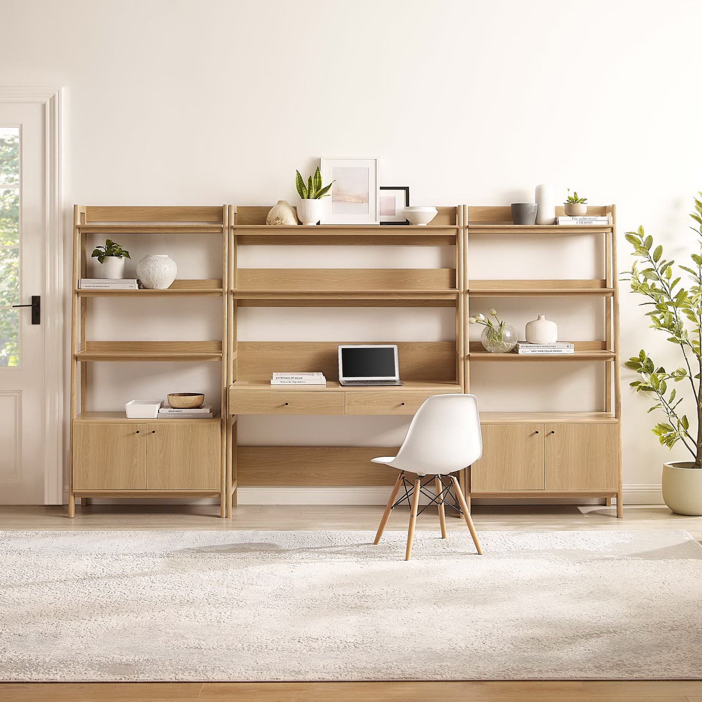 Brown oak modular desk-and-shelf unit with open shelves and lower cupboards, white chair, greenery