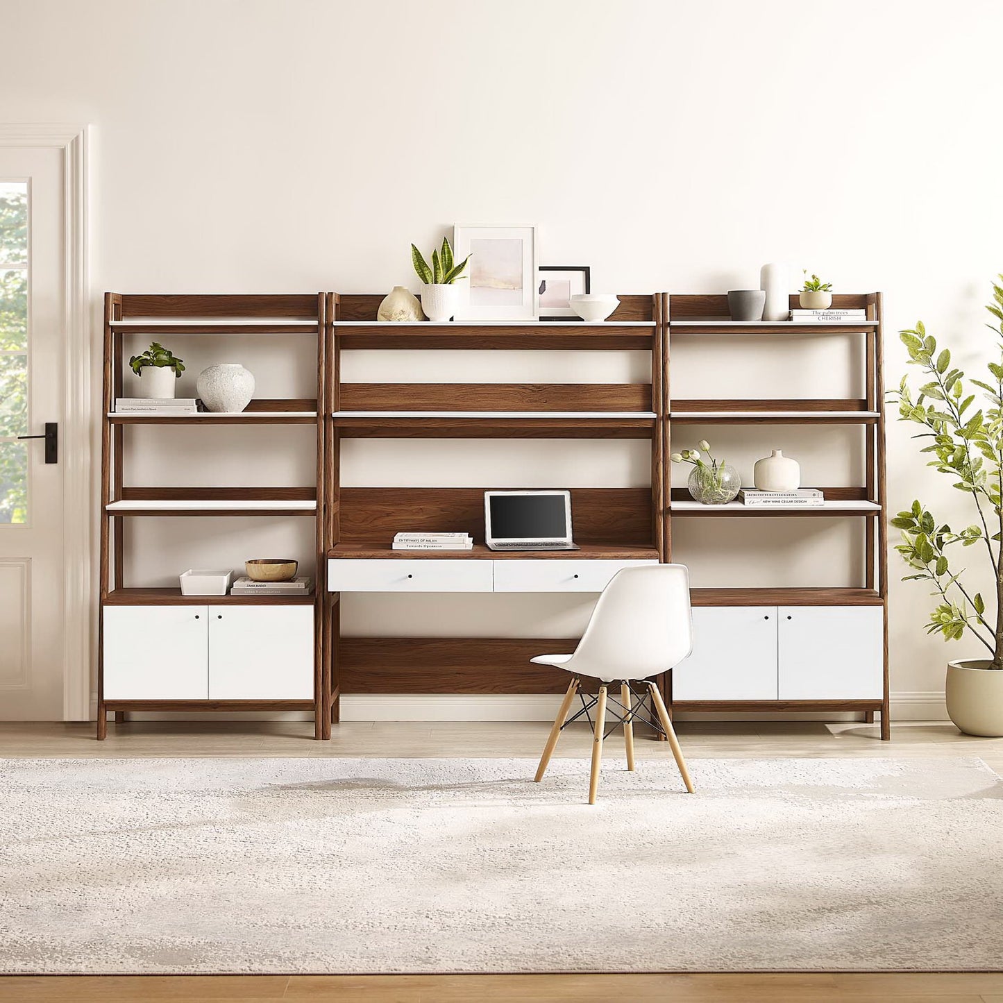 Walnut wood modular desk and bookshelf with white drawers, desk space for a laptop, and plants in a light modern home office.