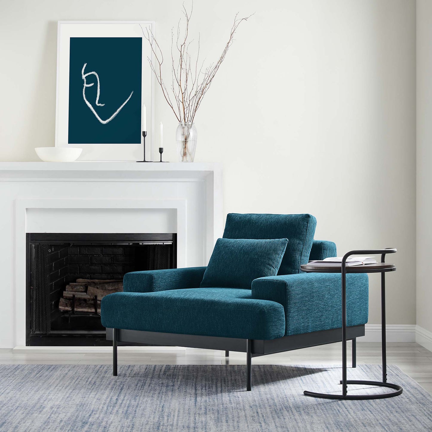 Teal blue upholstered armchair with square cushions and slim black metal legs, beside a round black side table.