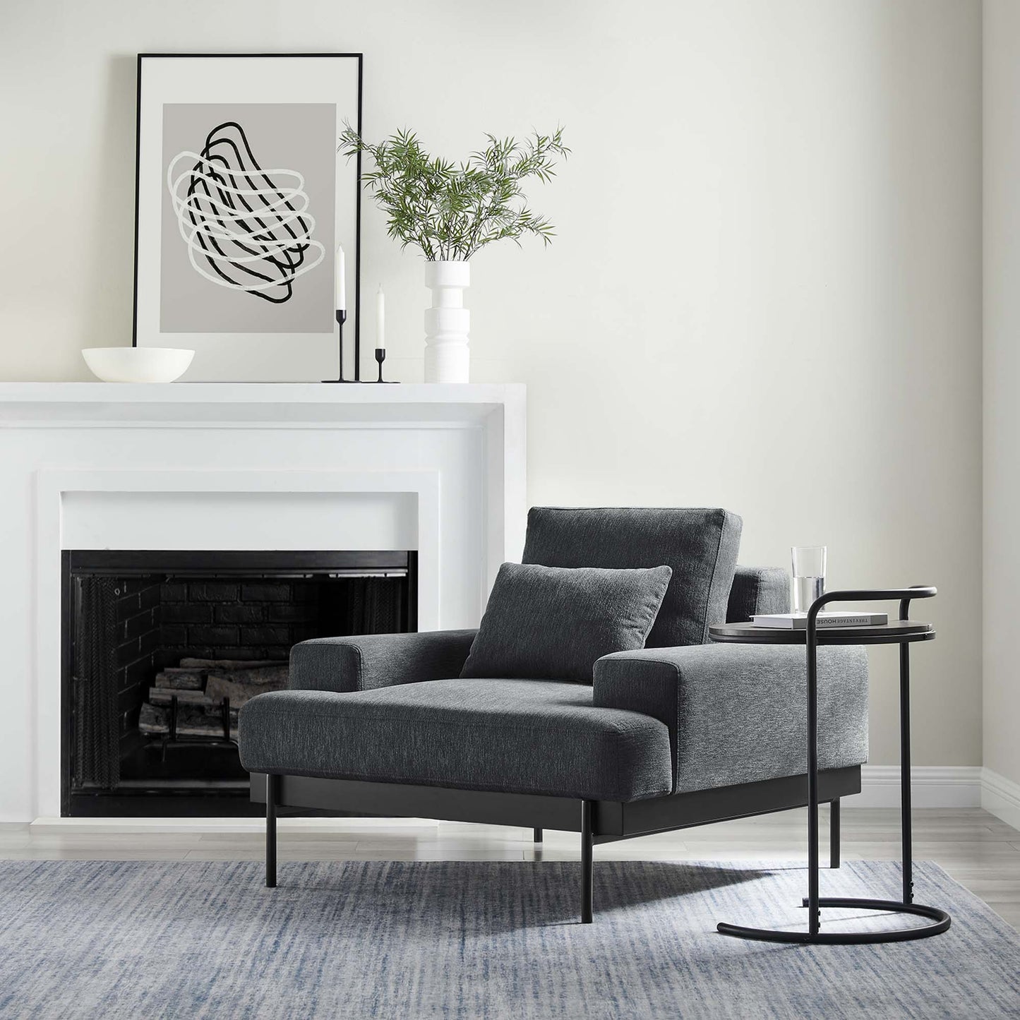 Charcoal gray fabric armchair with slim black legs and a matching cushion, next to a curved black metal side table.