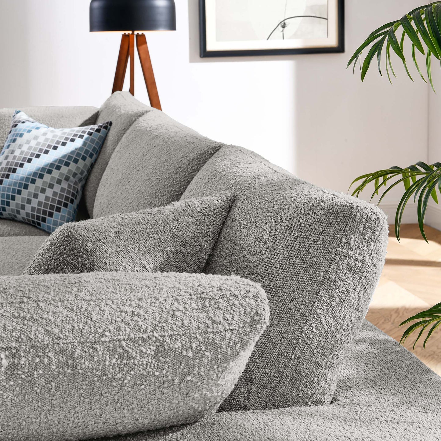Light gray textured sofa with matching cushions, blue geometric pillow, tripod lamp, framed art and greenery.