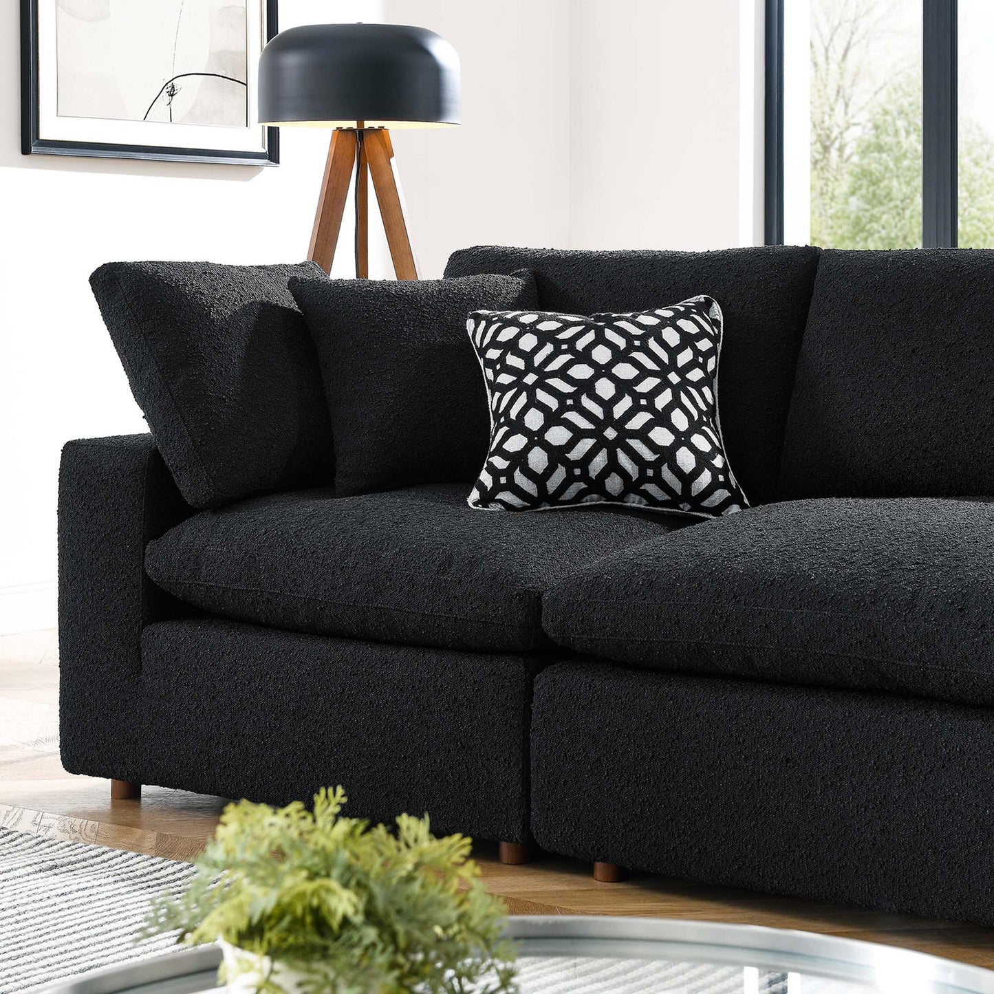 Charcoal textured boucle fabric 4-seater sofa (down-filled, overstuffed) with a black-and-white geometric pillow, wooden tripod floor lamp, and round glass coffee table.