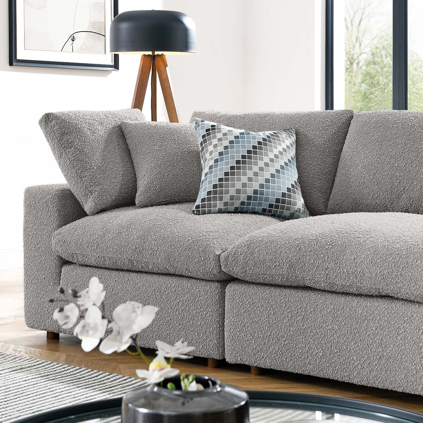 Light gray boucle sofa with textured cushions and a blue-gray geometric pillow in a bright modern living room.