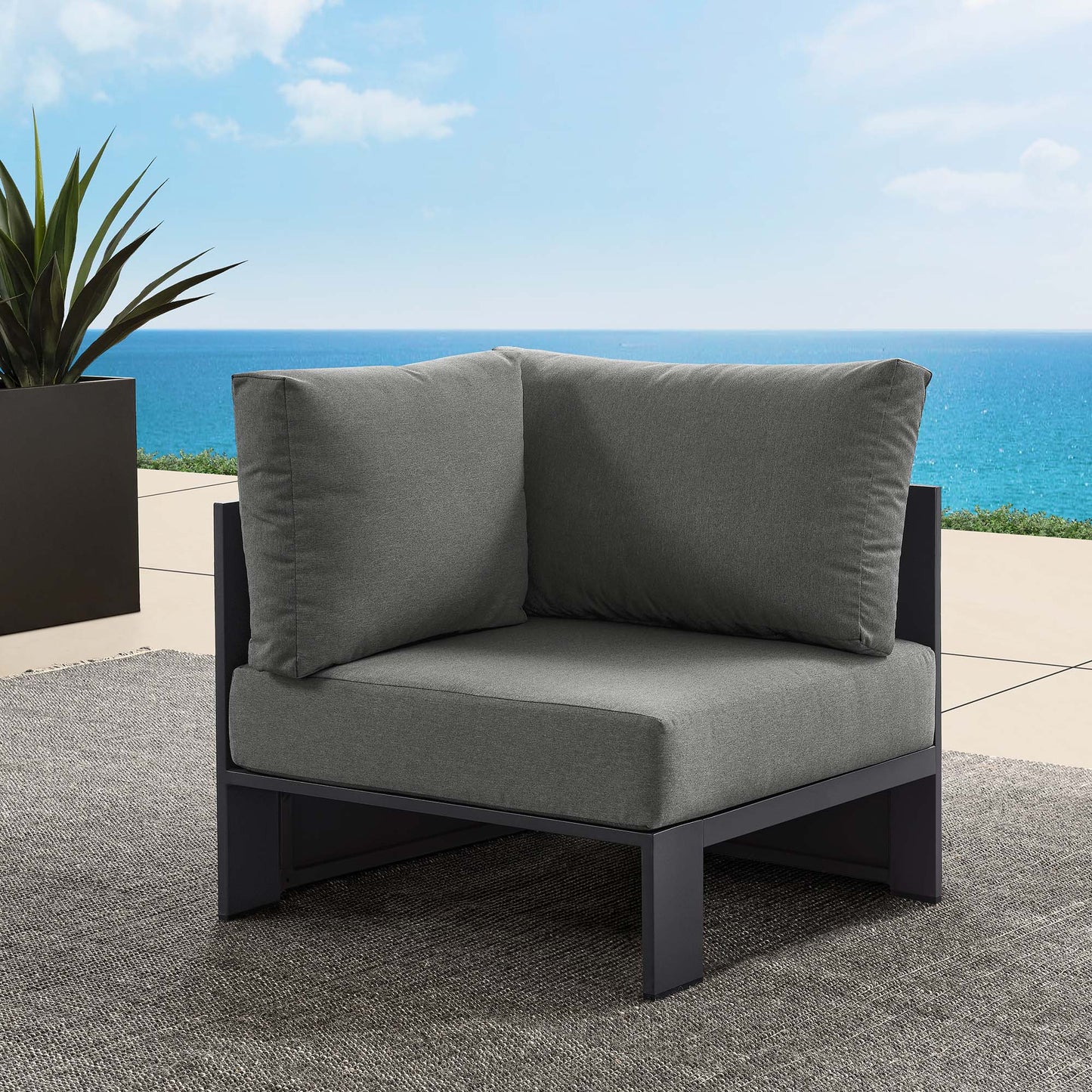 Grey outdoor modular corner chair with thick cushions on a dark metal frame, modern coastal patio.