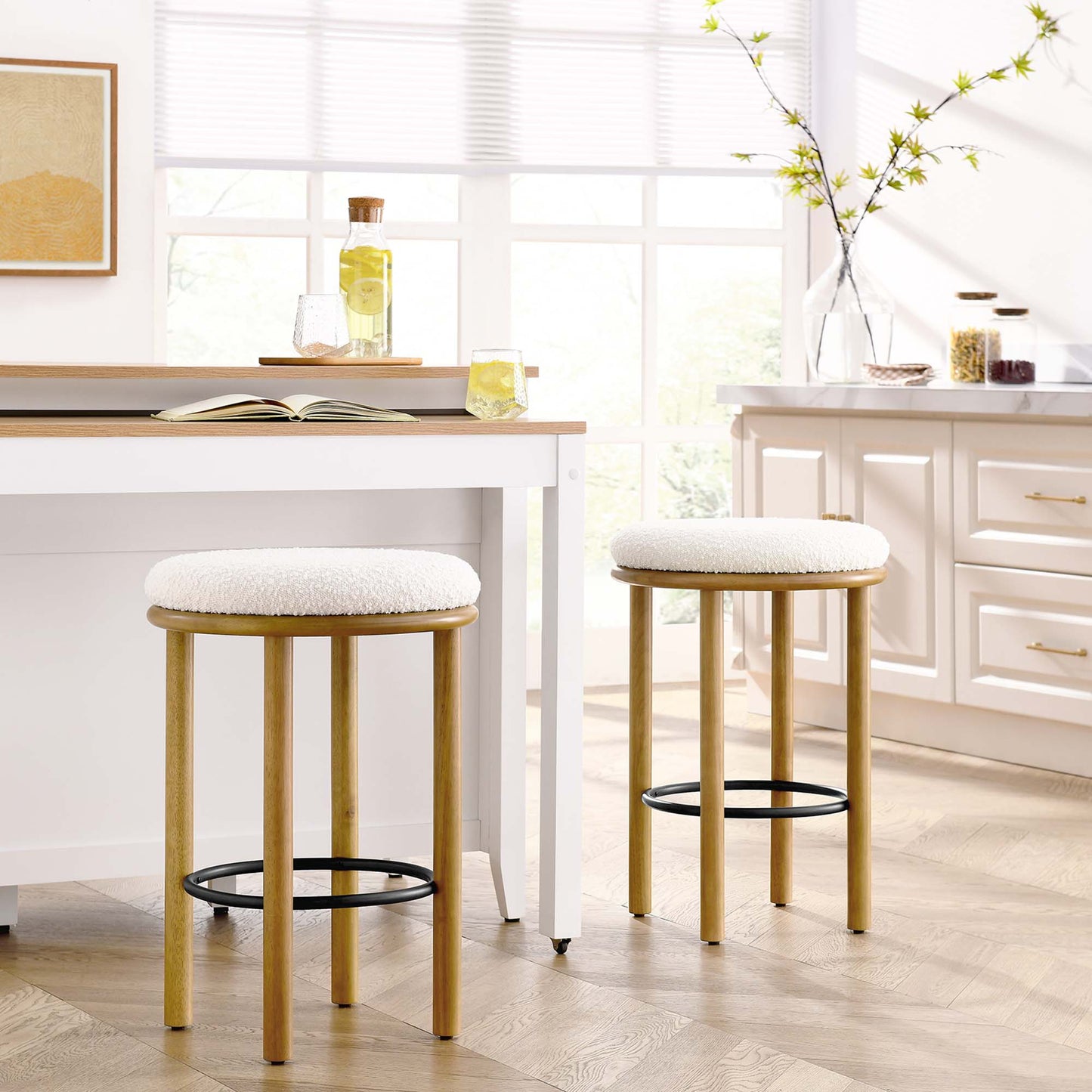 Oak bar stools with ivory boucle cushions and black footrests at a white kitchen island in a bright airy kitchen.