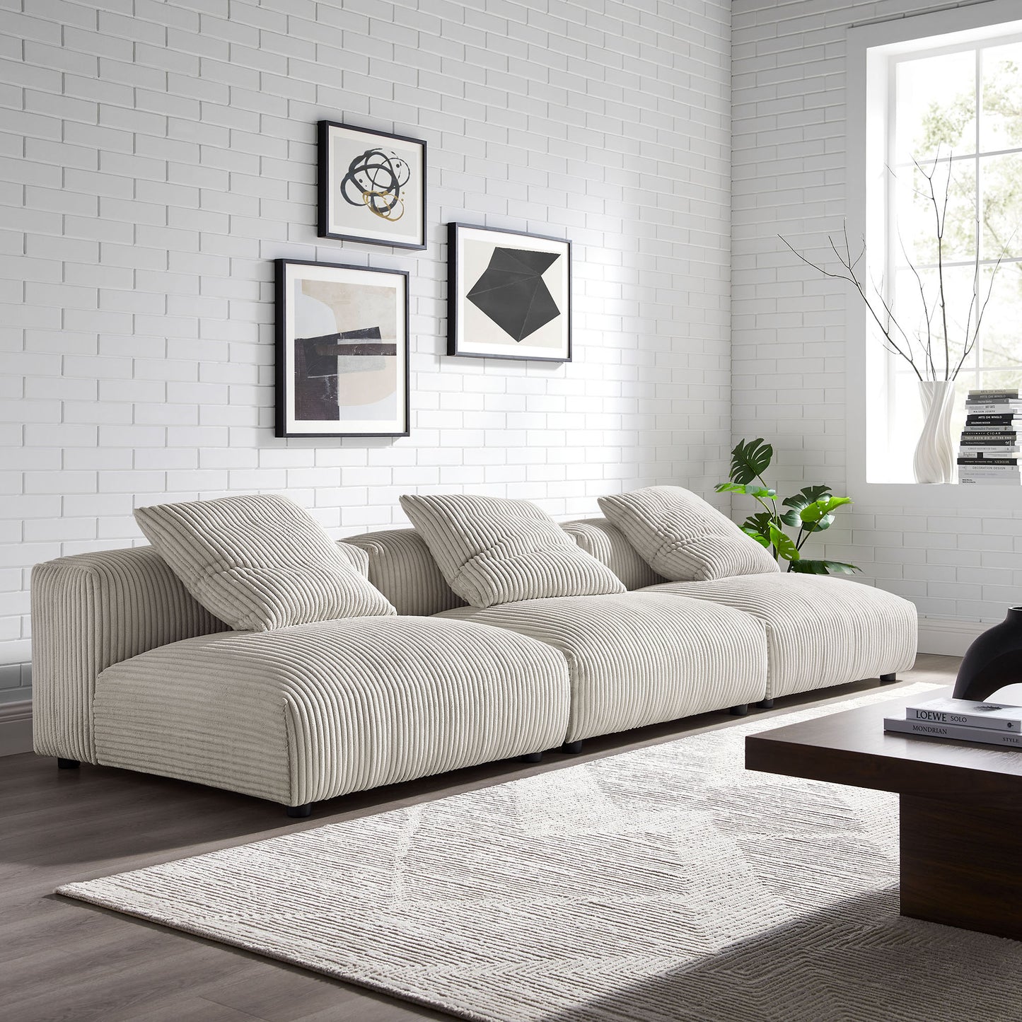 Brown corduroy 3-piece modular sofa in a white brick-walled living room with abstract wall art, gray rug, and a wooden coffee table.