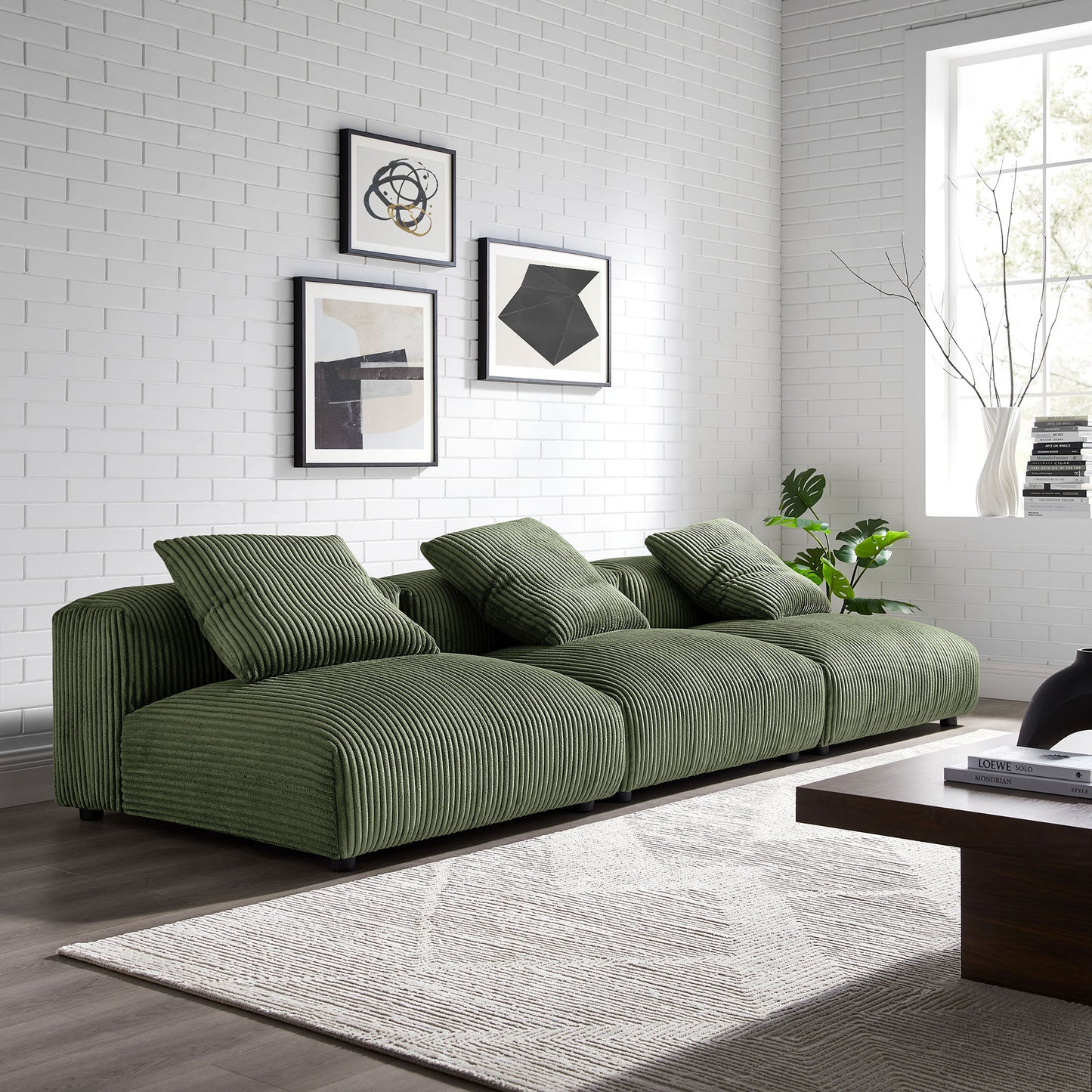 Olive green corduroy modular sofa in a white brick living room with abstract art, rug, and dark wood coffee table.
