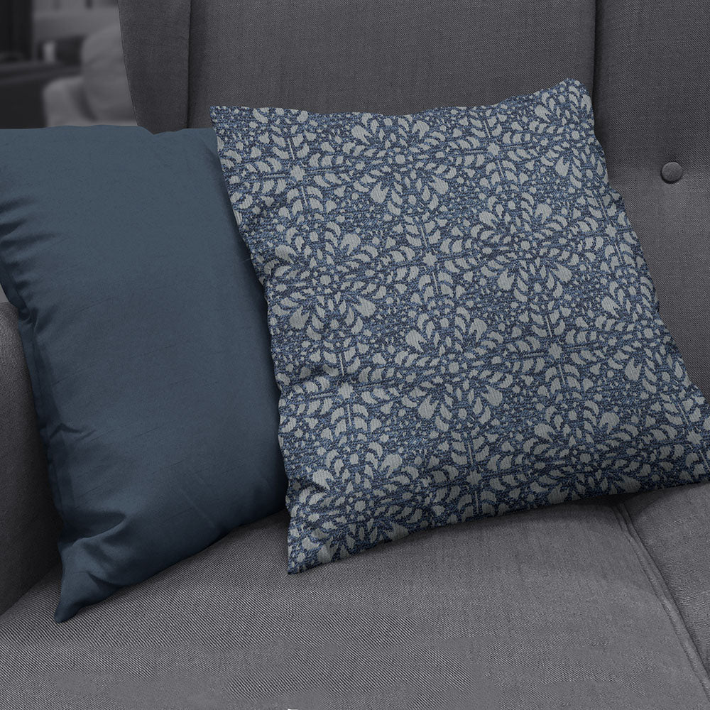 Two decorative throw pillows on a grey sofa: solid blue cushion and blue floral lattice patterned cushion.