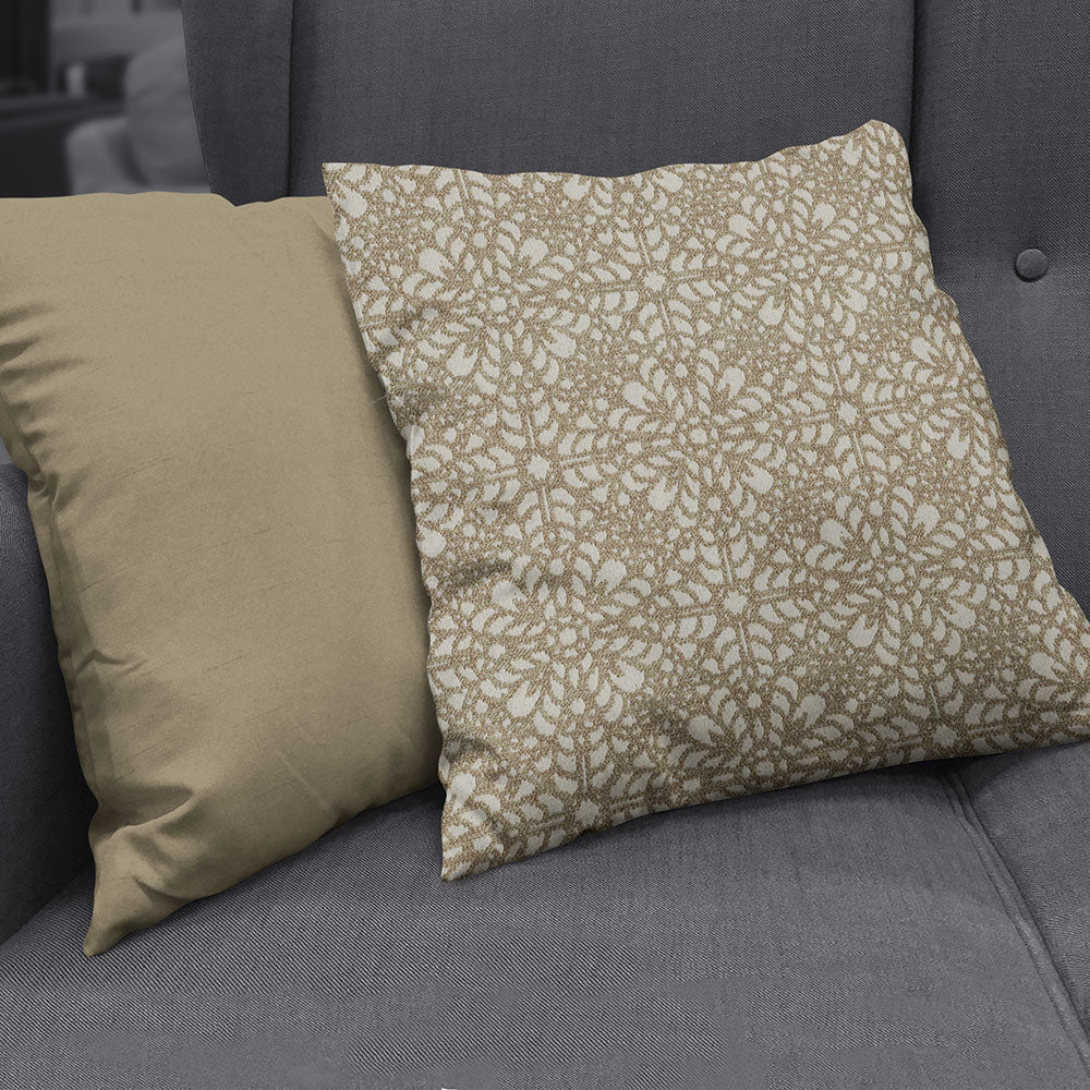Two decorative throw pillows on a dark grey sofa; solid beige pillow beside a beige-and-white floral patterned cushion.