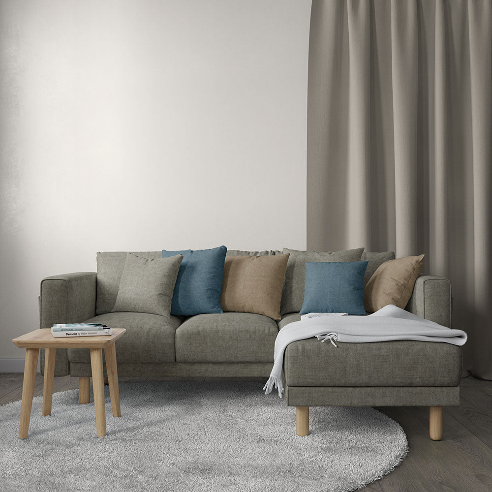 Grey sectional sofa with blue and tan cushions, chaise on the right, light wood legs, round coffee table and soft rug.