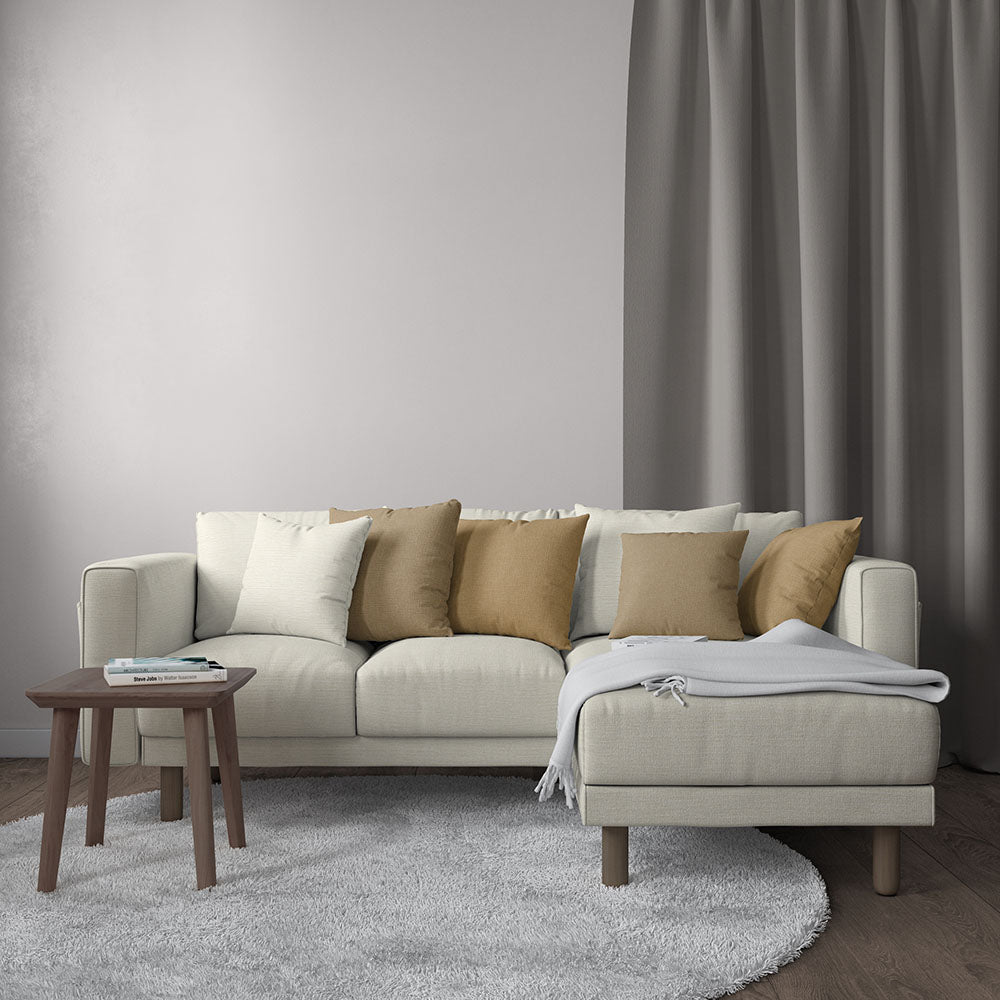 Beige sectional with chaise, cream & tan cushions, gray throw blanket; round wooden coffee table in a neutral living room