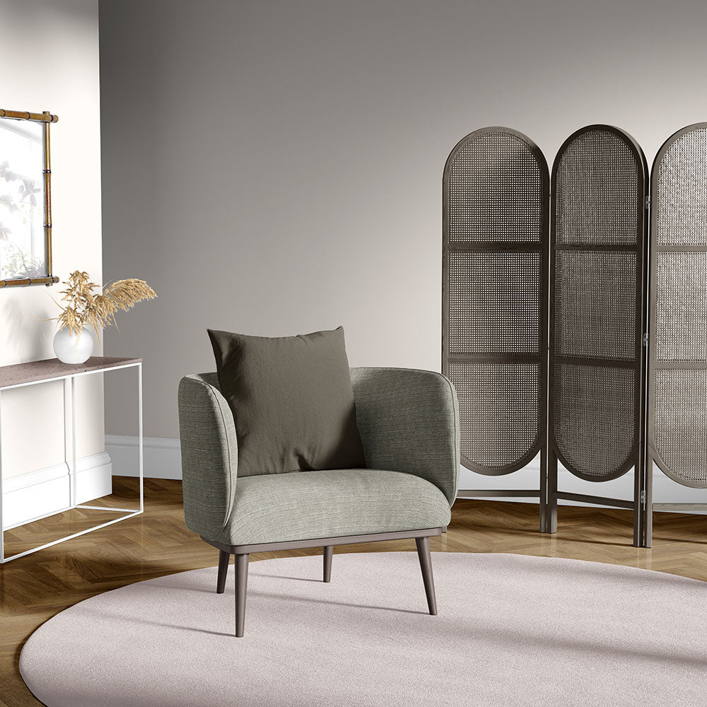 Gray mid-century armchair with wood legs, brown cushion, in a neutral living room with a woven room divider and round rug.