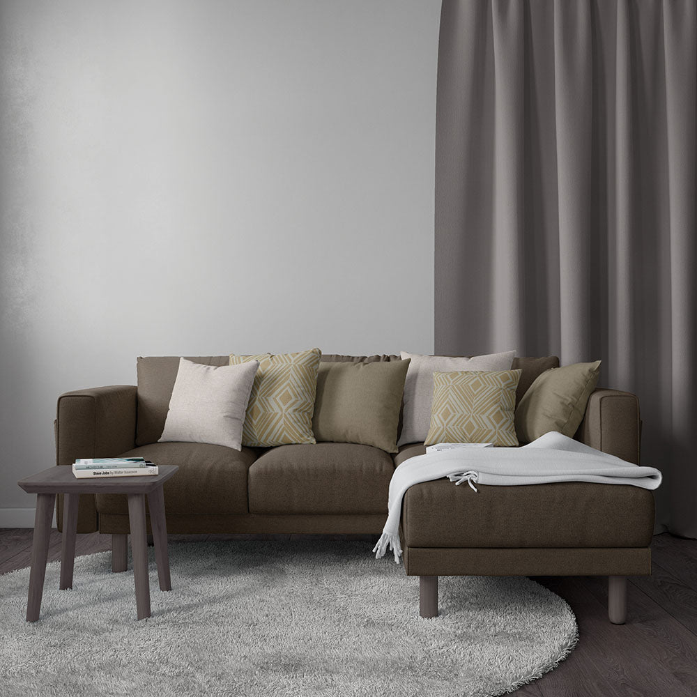 Brown sectional sofa with beige and patterned cushions, chaise with white throw, wooden side table, grey rug and curtains.