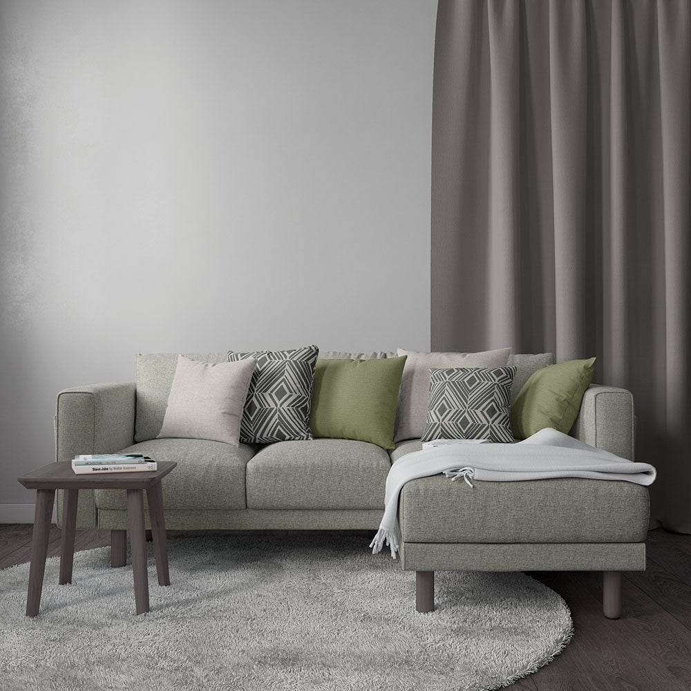 Light gray modular sofa with green and gray cushions, pink accent, gray throw, round dark wood side table, taupe drapes.