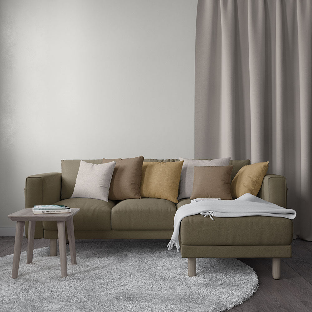 Olive-tan fabric sectional with chaise, neutral throw pillows, light wood legs, round side table, gray rug and curtains.