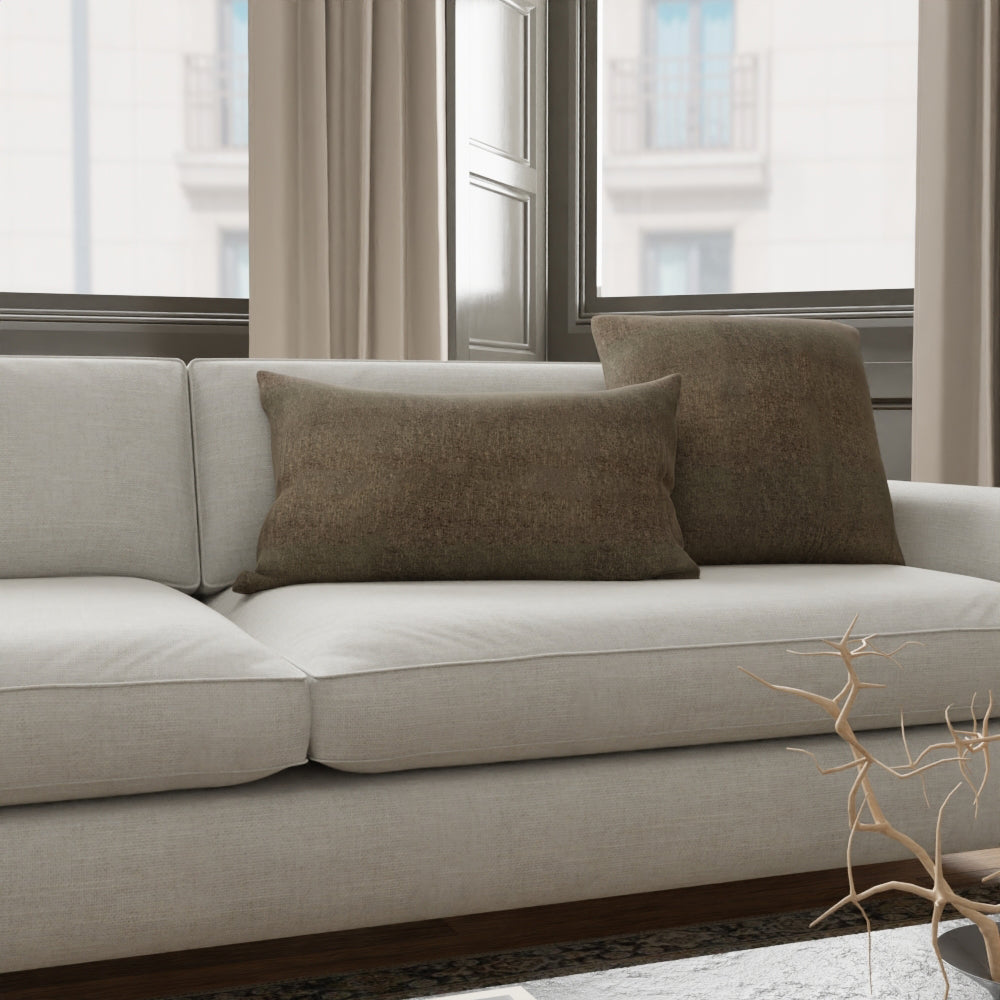 Light gray fabric sofa with two brown cushions in a bright living room by large windows; bare branch decor in foreground.