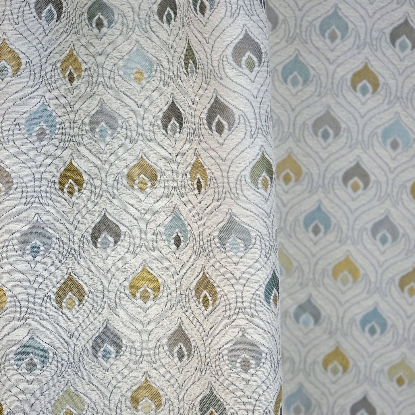 Roll of jacquard fabric featuring a repeating flame/teardrop motif in blue, teal, yellow, & olive on white.