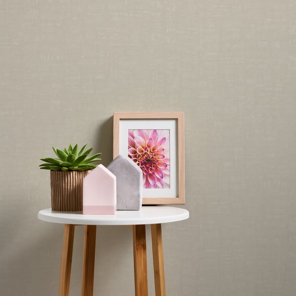 Beige linen-effect textured wallpaper backdrop; pastel decor scene with a succulent in a ribbed pot, pastel house shapes, and a framed pink floral art.
