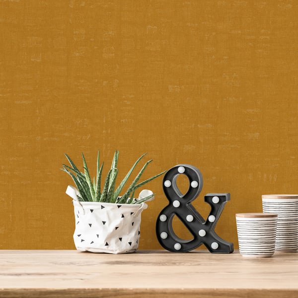 Gold linen-effect textured wallpaper background; foreground features a white planter with a green succulent, black marquee ampersand, and striped cups on a wood surface.