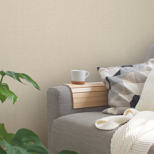 Gray fabric sofa with a light wood slatted armrest tray and white mug; geometric pillows and a cream knit blanket.