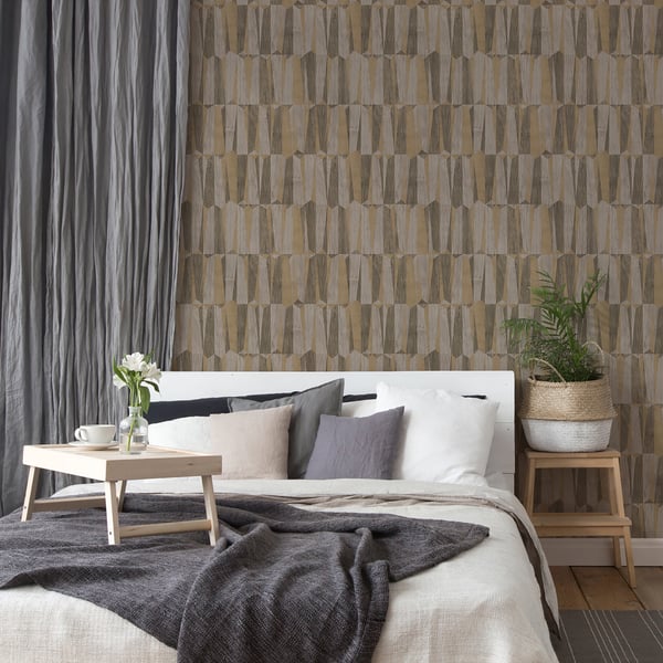 Neutral-toned bedroom with white bed, beige/gray cushions, dark throw, wooden tables, and geometric wallpaper.
